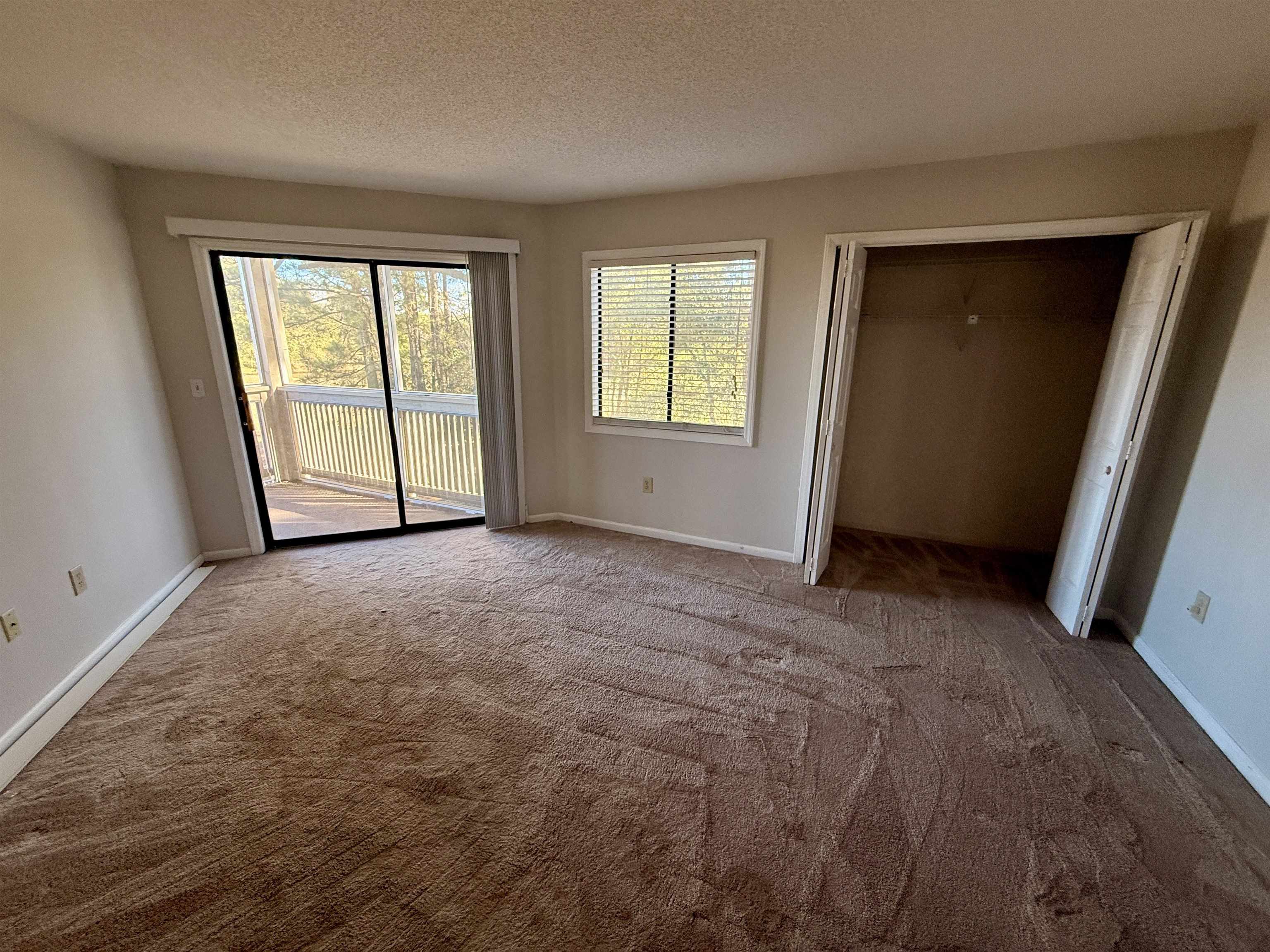 4230 Pinehurst Circle, Unit K4 Little River, SC 29566 - Photo 7 of 25 Unfurnished bedroom featuring access to exterior, carpet flooring, a closet, multiple windows, and a textured ceiling