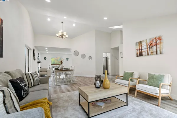 a living room with furniture two large window and wooden floor