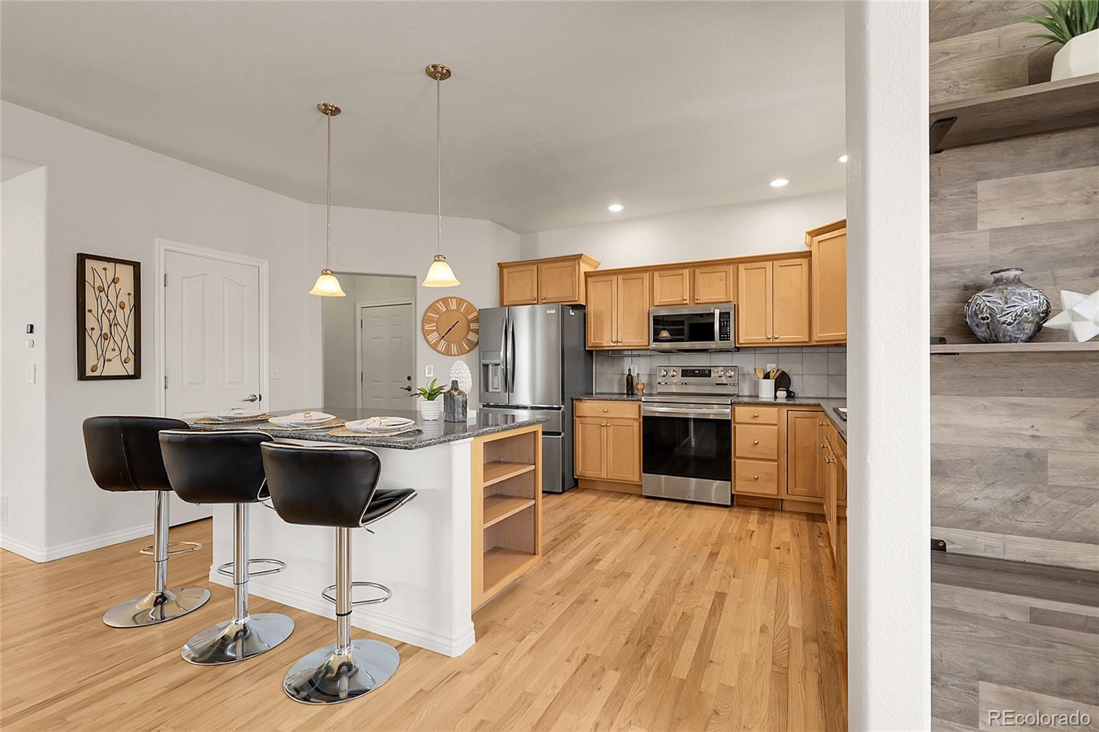 3406 Purcell Street Brighton, CO 80601 - Photo 15 of 50 a kitchen with stainless steel appliances kitchen island granite countertop a refrigerator a stove a kitchen island a dining table and chairs with wooden floor