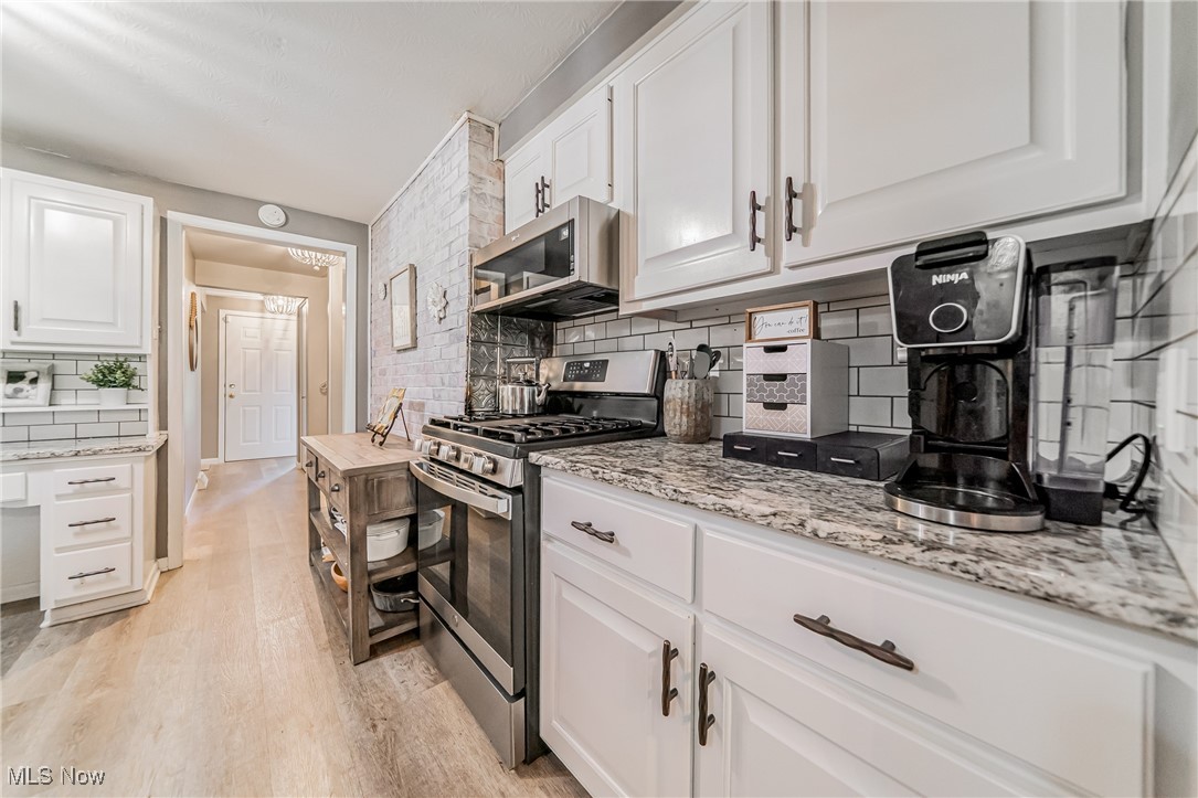 595 Moorfield Road Fairlawn, OH 44313 - Photo 10 of 50 Kitchen featuring backsplash, stainless steel appliances, white cabinets, light wood-style floors, and light stone counters