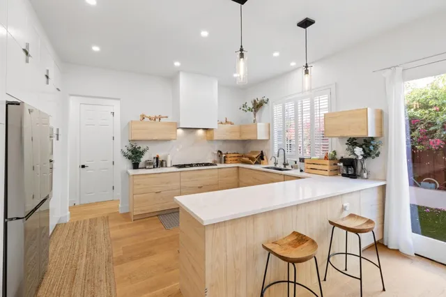 a view of a kitchen with kitchen island a stove a refrigerator a sink and a dining table with wooden floor