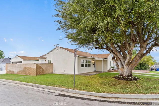 a view of a white house next to a yard with a large tree