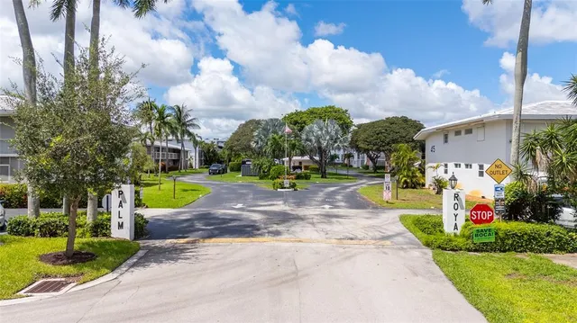 a view of a fountain in front of a house with a big yard and potted plants