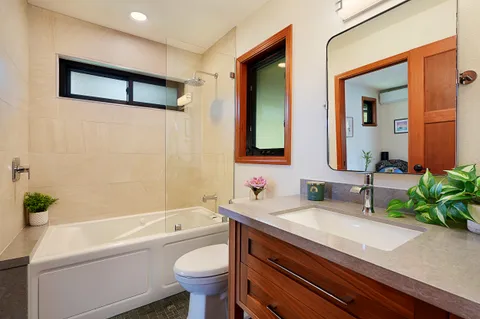 a bathroom with a granite countertop sink a toilet a mirror a vanity a bathtub and shower