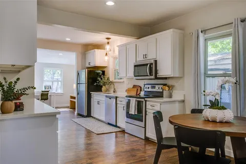 a kitchen with stainless steel appliances a stove a sink a microwave a refrigerator white cabinets and wooden floor