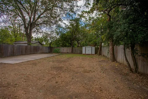 a view of a backyard with large trees and wooden fence