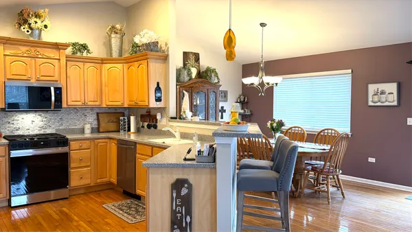a kitchen with stainless steel appliances granite countertop a stove top oven a sink a dining table and chairs with wooden floor