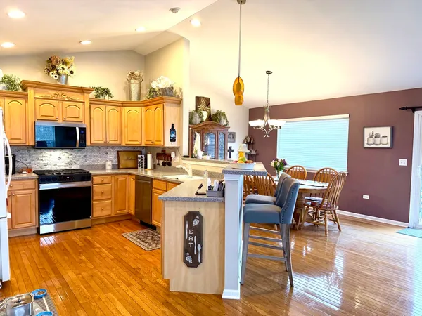 a kitchen with stainless steel appliances granite countertop a stove top oven a sink a dining table and chairs with wooden floor