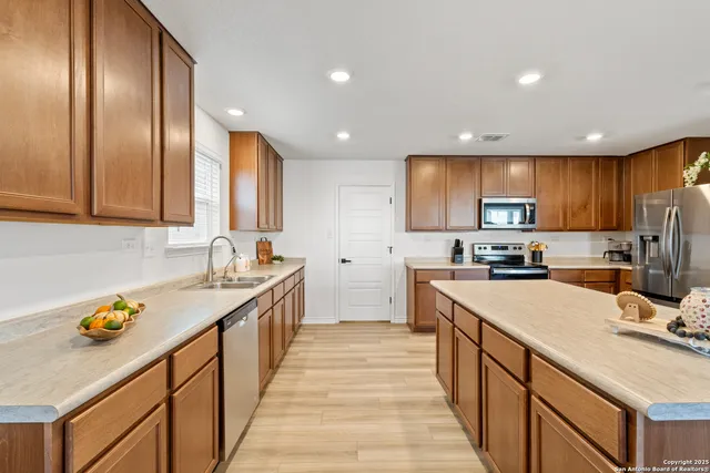 a kitchen with stainless steel appliances granite countertop wooden cabinets a sink dishwasher a stove and a refrigerator with wooden floor