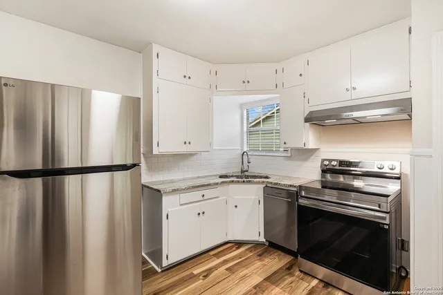 a kitchen with granite countertop a refrigerator stove and white cabinets