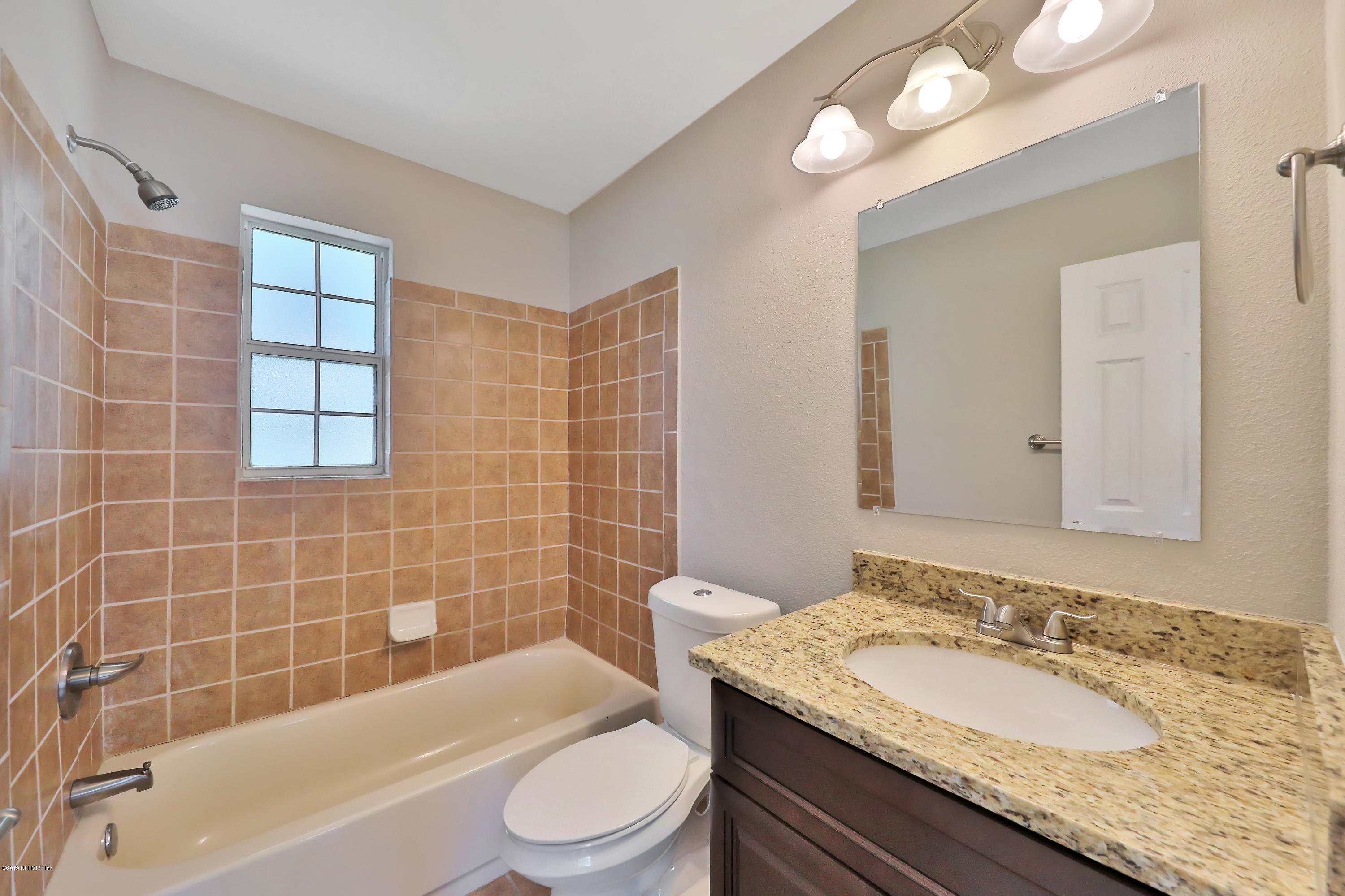 2932 Mansion Road Jacksonville, FL 32277 - Photo 17 of 22 a bathroom with a granite countertop sink a toilet a mirror a bathtub and shower