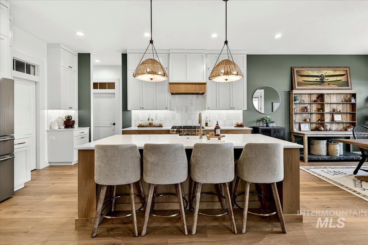 24853 Haflinger Way Middleton, ID 83644 - Photo 15 of 49 Kitchen featuring a breakfast bar area, light wood-style floors, a center island with sink, pendant lighting, and two tone cabinetry