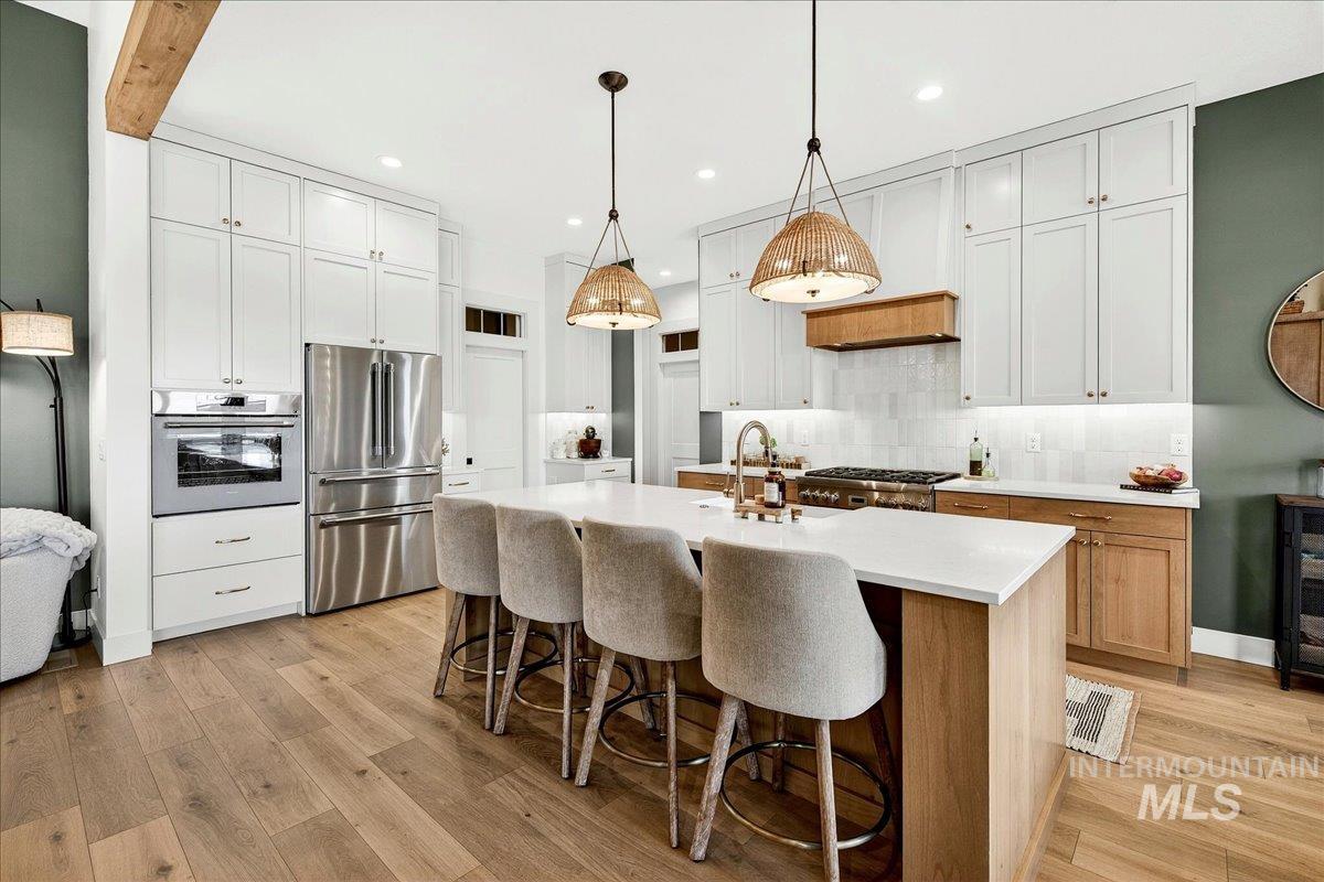 24853 Haflinger Way Middleton, ID 83644 - Photo 17 of 49 Two tone kitchen with stainless steel appliances, a center island with sink, a kitchen breakfast bar, pendant lighting, and light wood-style flooring