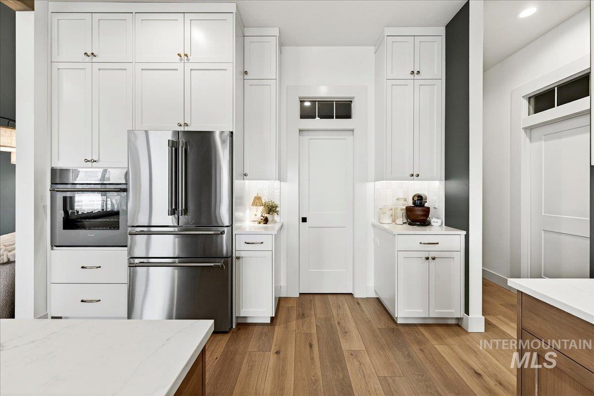 24853 Haflinger Way Middleton, ID 83644 - Photo 18 of 49 Kitchen featuring stainless steel appliances, light wood-style floors, white cabinets, light stone countertops, and recessed lighting