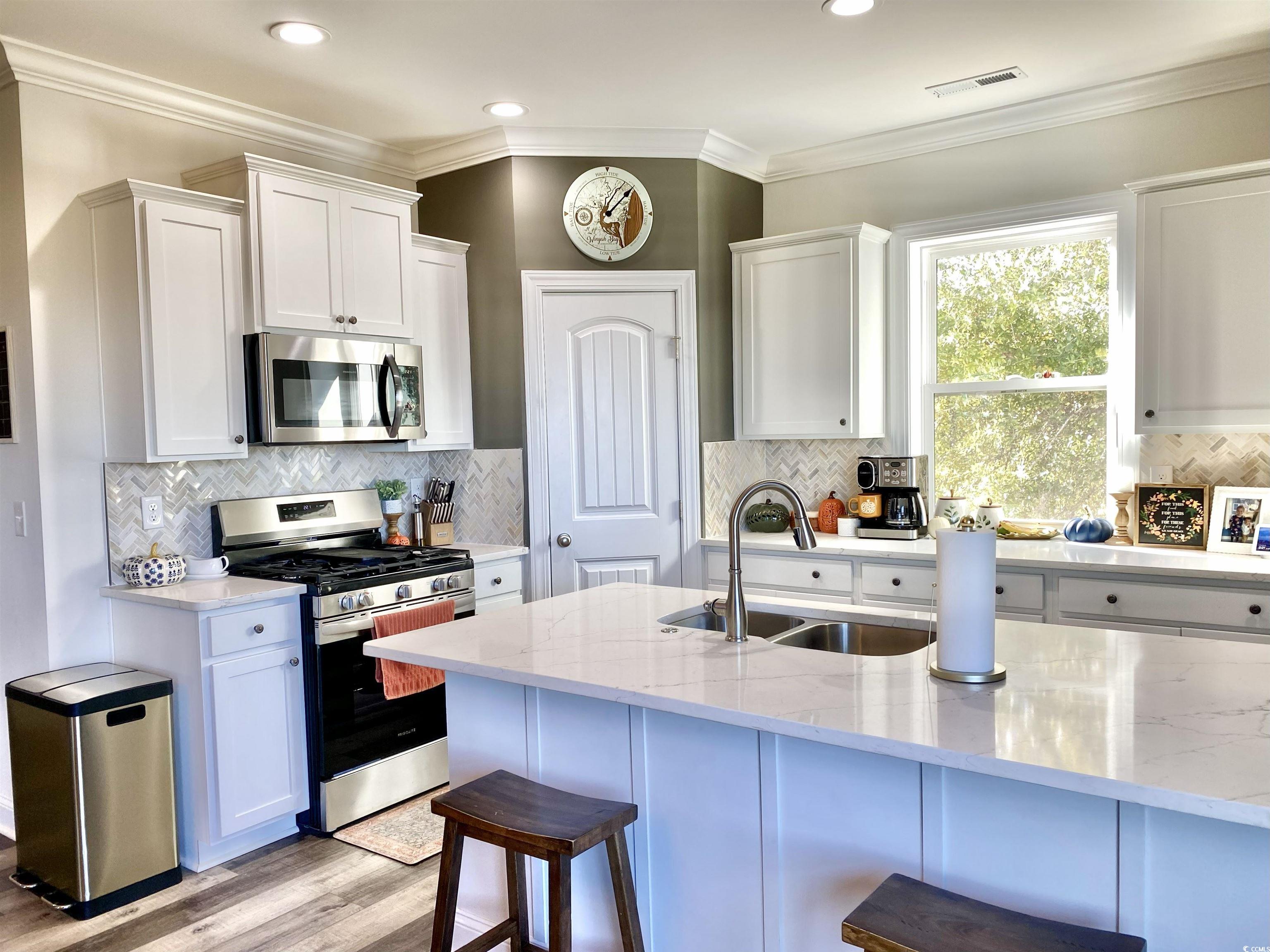 2664 Seaport Circle Georgetown, SC 29440 - Photo 11 of 40 Kitchen featuring ornamental molding, appliances with stainless steel finishes, white cabinetry, light stone countertops, and tasteful backsplash