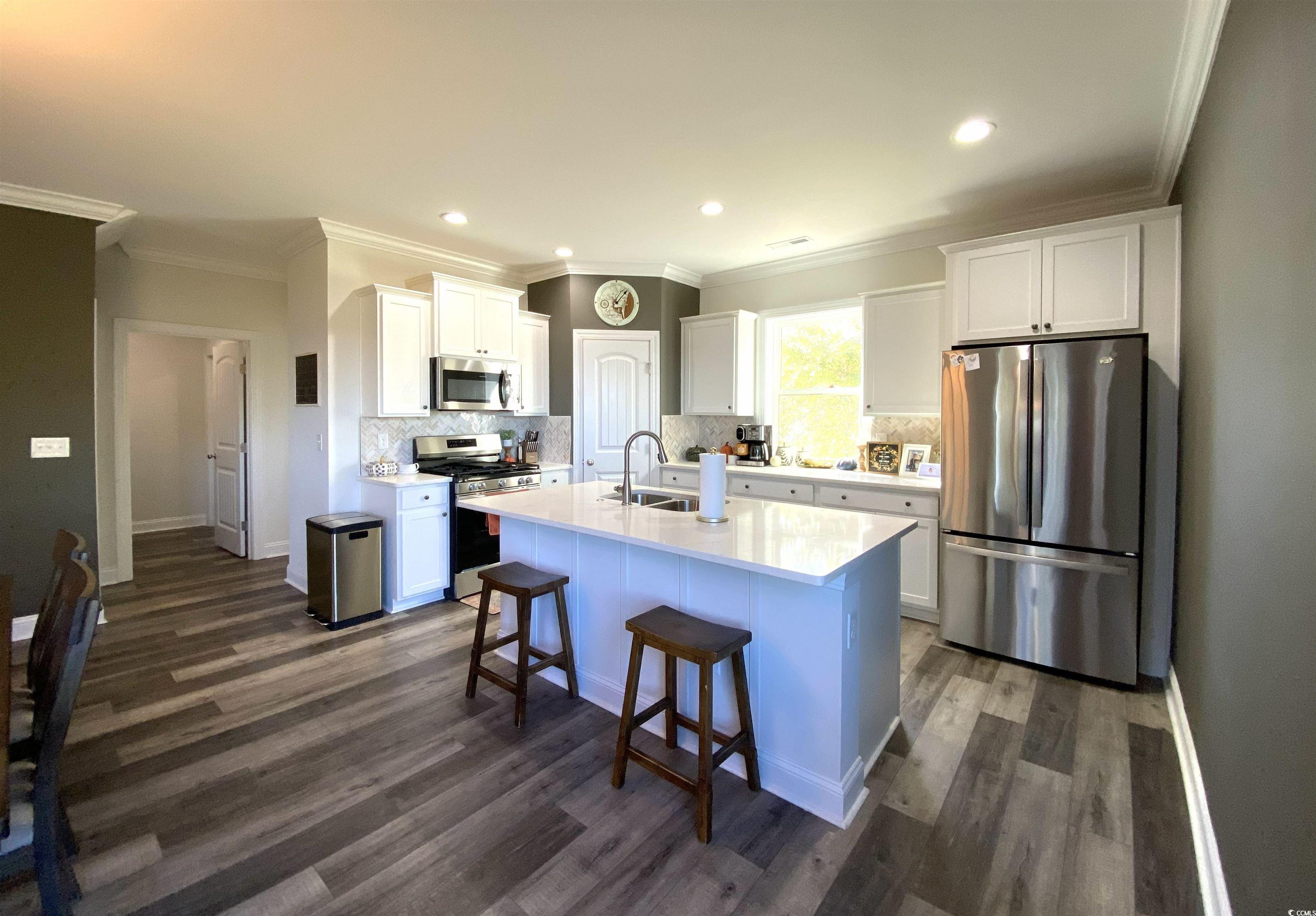 2664 Seaport Circle Georgetown, SC 29440 - Photo 15 of 40 Kitchen featuring appliances with stainless steel finishes, crown molding, white cabinets, decorative backsplash, and a kitchen breakfast bar