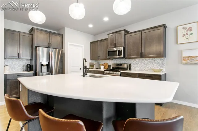 a kitchen with stainless steel appliances a dining table chairs refrigerator and sink