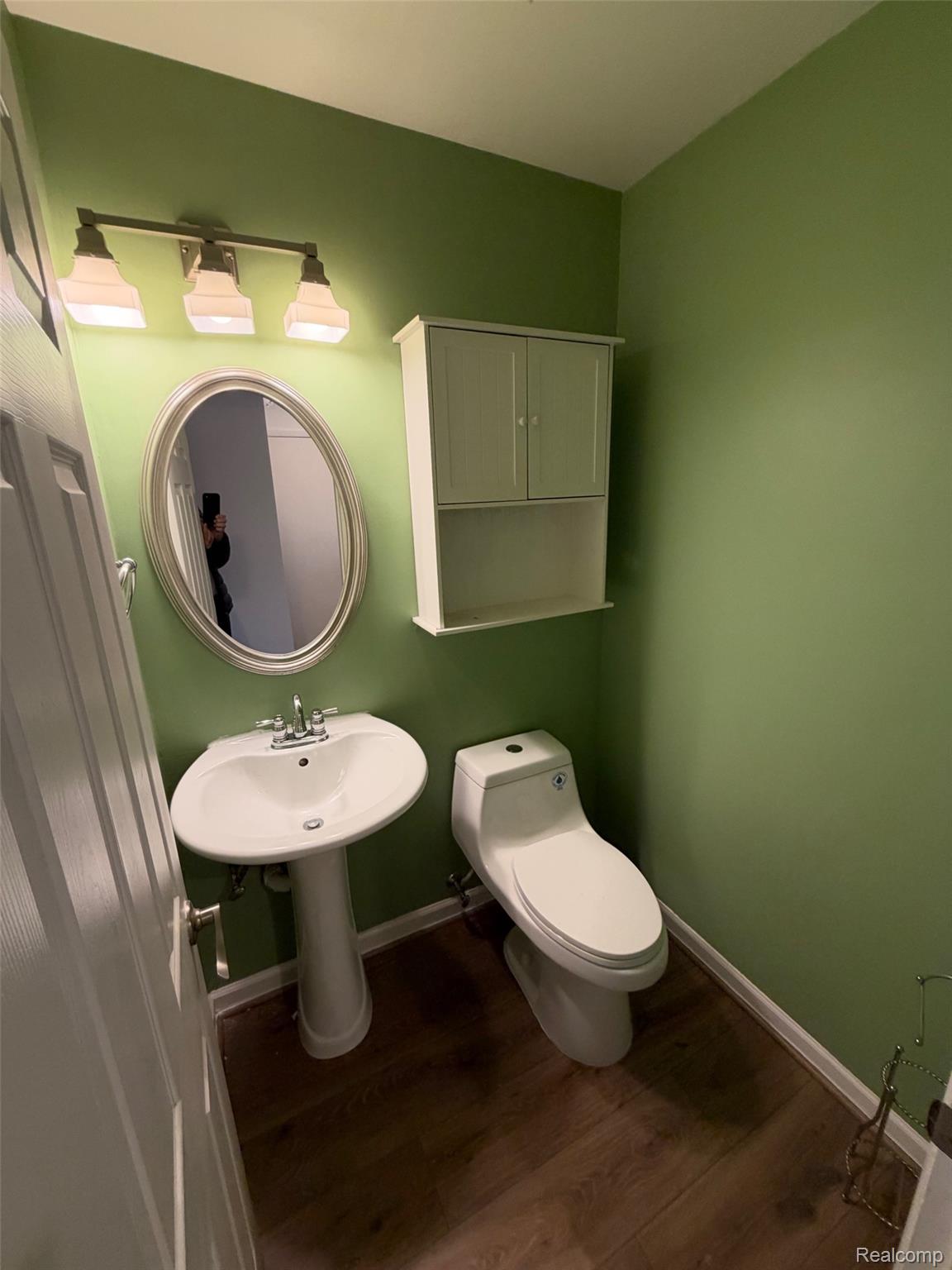 24525 Jamestowne Road Novi, MI 48375 - Photo 11 of 20 Pedestal sink with chrome faucet, oval mirror, wall-mounted cabinet, and wood-finish flooring