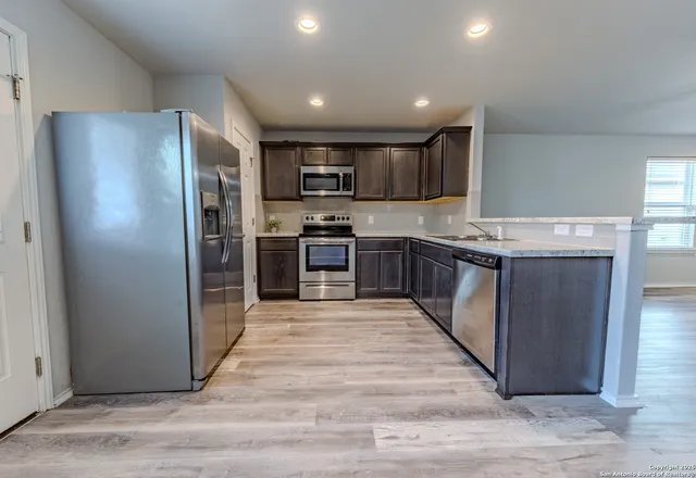 a large kitchen with stainless steel appliances granite countertop a stove top oven a refrigerator and a sink