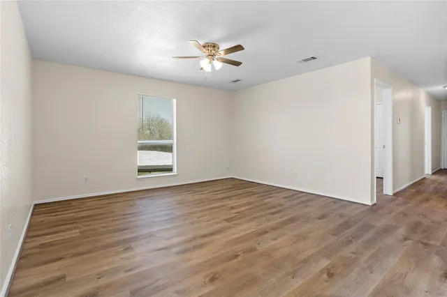 an empty room with wooden floor chandelier fan and windows
