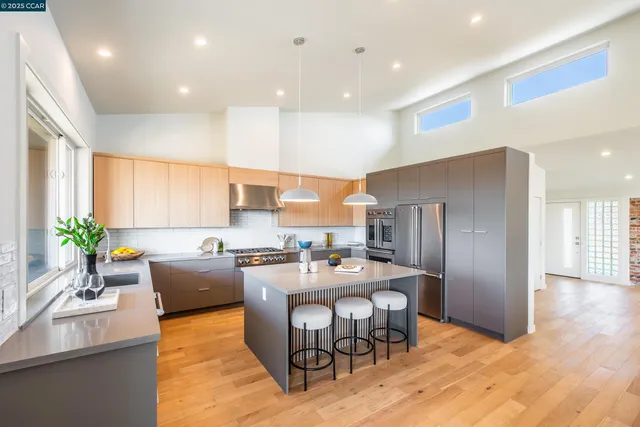 a kitchen with stainless steel appliances kitchen island granite countertop a refrigerator a sink a stove a dining table and chairs