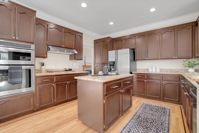 a kitchen with stainless steel appliances granite countertop a stove top oven a sink dishwasher and a refrigerator with wooden cabinets