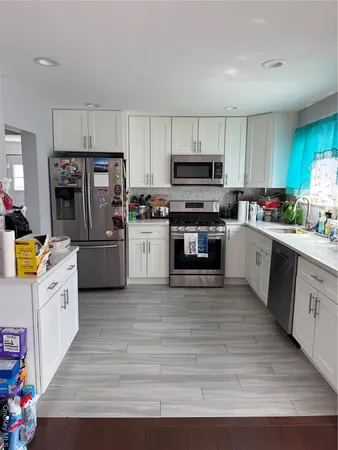 a kitchen with stainless steel appliances a stove top oven a microwave a refrigerator a sink dishwasher and white cabinets with wooden floor