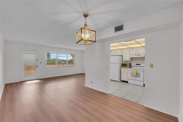 an empty room with wooden floor kitchen view and a window