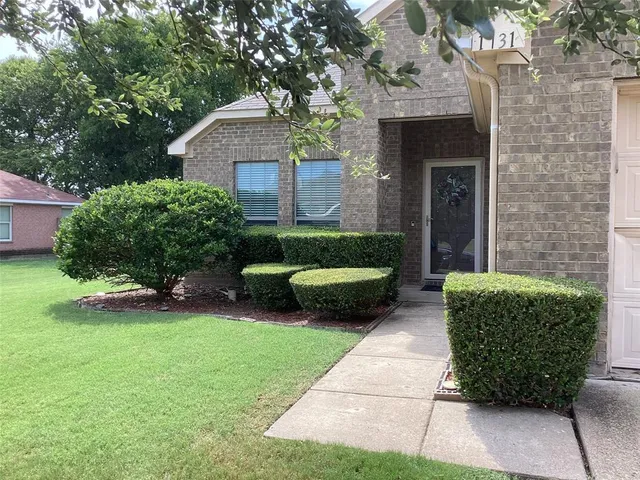 a view of a house with a yard plants and a large tree