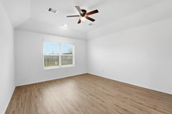 an empty room with wooden floor ceiling fan and window