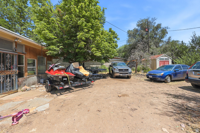 5480 South 2000th Street West Roy, UT 84067 - Photo 29 of 36 Expansive dirt lot providing ample outdoor parking, featuring a rustic wooden shed with red double doors, and mature trees providing natural shade