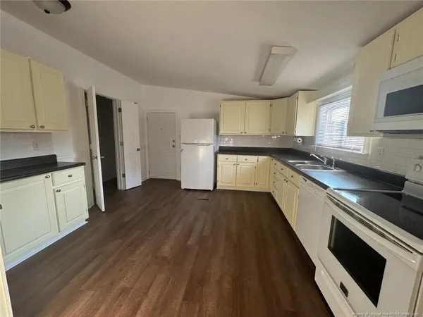 a kitchen with granite countertop a refrigerator a sink dishwasher a stove and white cabinets with wooden floor