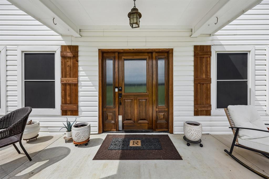 331 Radecke Road Krum, TX 76249 - Photo 6 of 40 Inviting front porch featuring white siding, a solid wood entry door with sidelights, coordinating wood shutters, and an overhead lantern-style light fixture