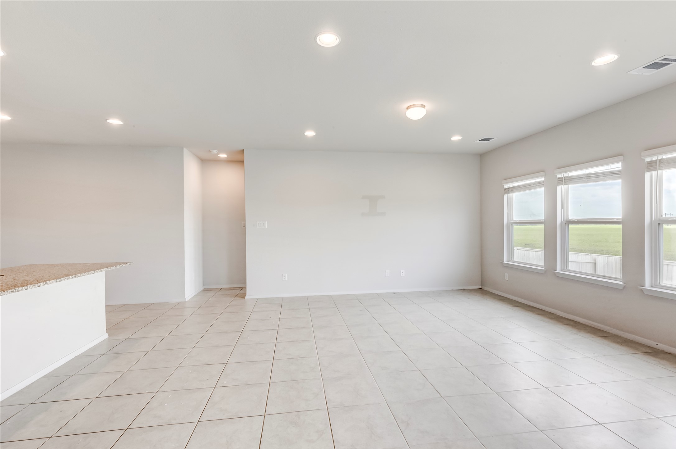 2721 Winding Creek Road Kyle, TX 78640 - Photo 4 of 27 Spacious interior room featuring light-colored tile flooring, multiple windows providing natural illumination, recessed ceiling lights, a central ceiling light fixture, and a built-in counter with a speckled surface