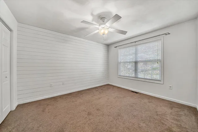 an empty room with chandelier fan and windows