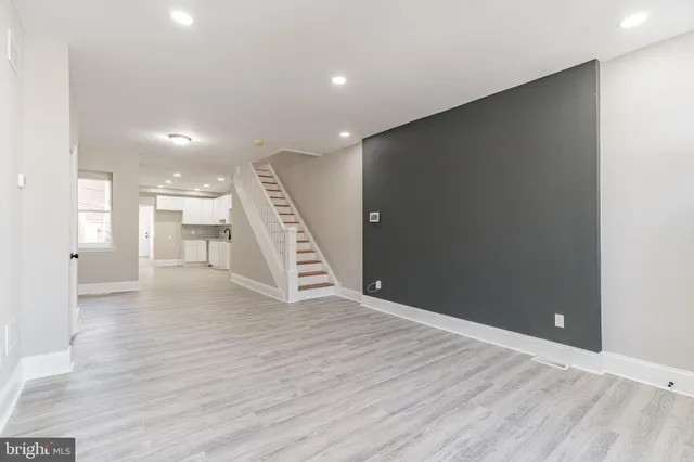 a view of an empty room with wooden floor and a kitchen