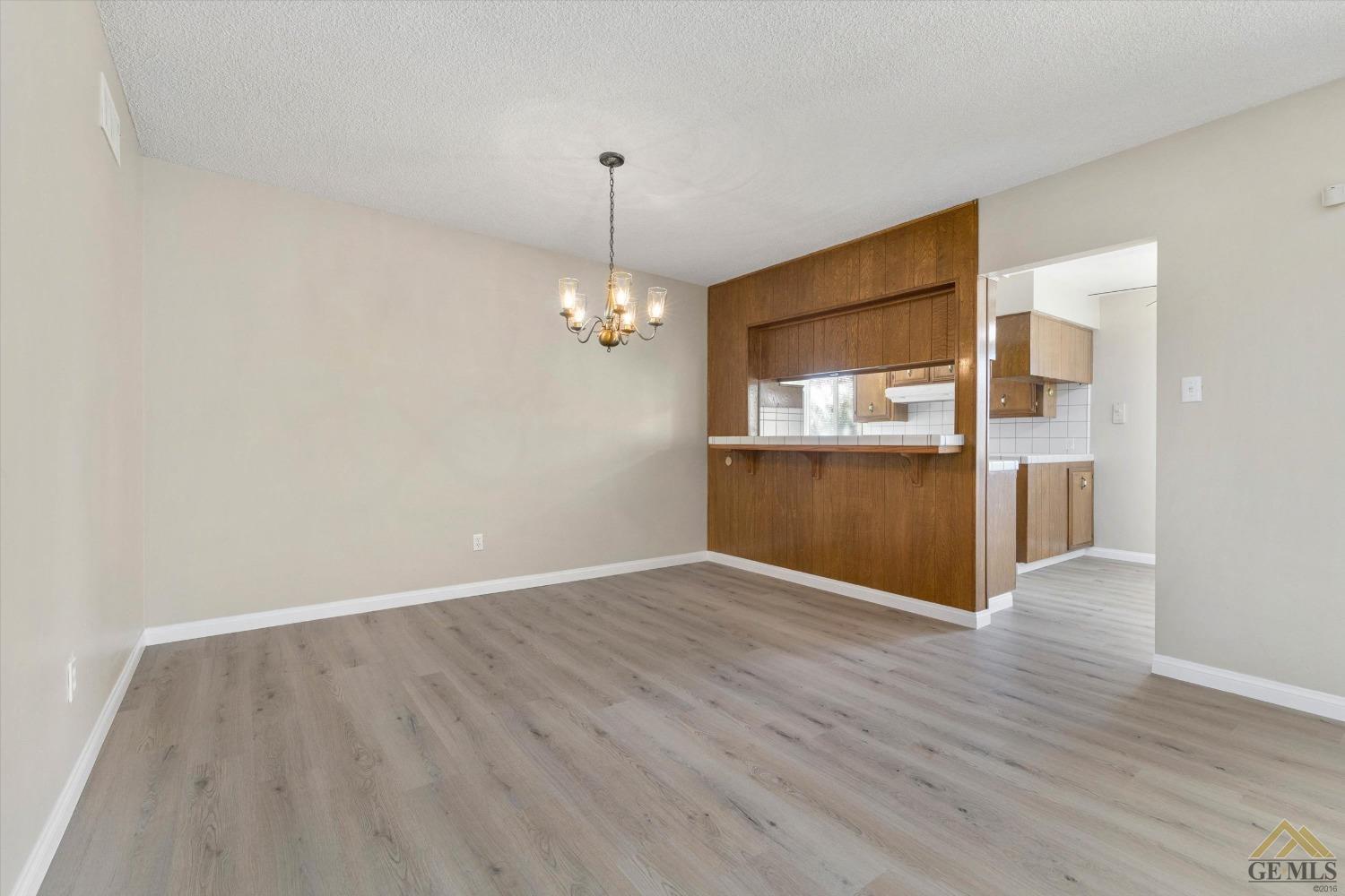 Undisclosed Address Bakersfield, CA 93309 - Photo 12 of 32 an empty room with wooden floor kitchen view and a chandelier
