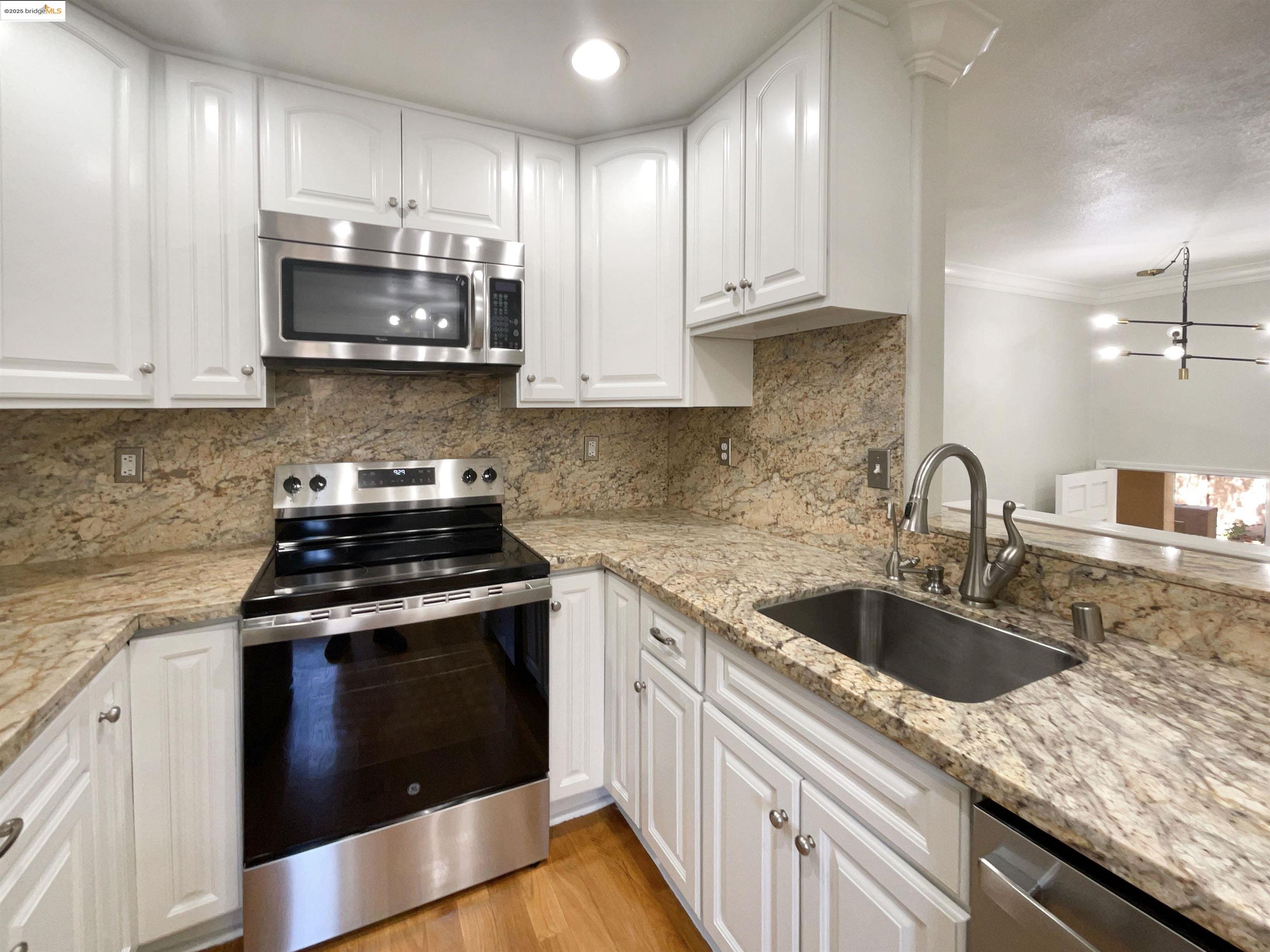 991 Asilomar Terrace, Unit 1 Sunnyvale, CA 94086 - Photo 14 of 20 Kitchen with appliances with stainless steel finishes, ornamental molding, white cabinetry, light wood-style flooring, and light stone counters