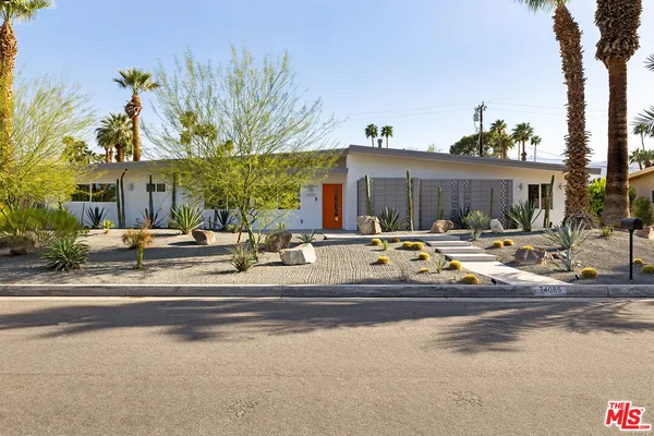 a view of a brick house with large windows and palm trees