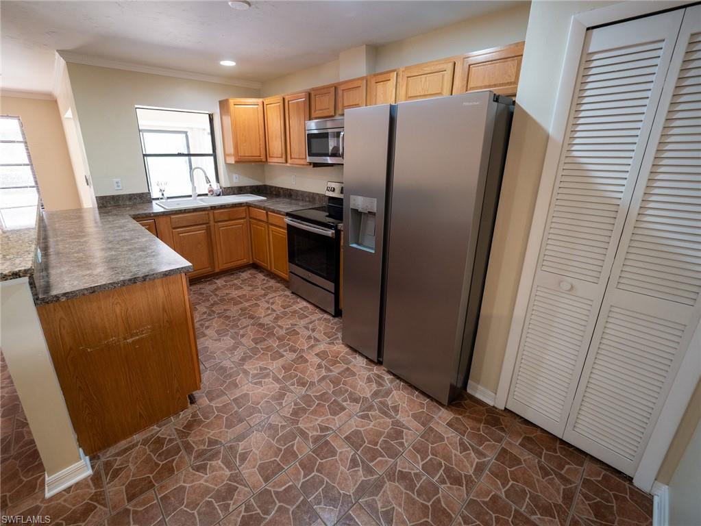 18414 Tulip Road Fort Myers, FL 33967 - Photo 8 of 37 Kitchen featuring L-shaped wood cabinetry with coordinating countertops, stainless steel appliances, a double basin sink under a window, and patterned tile flooring