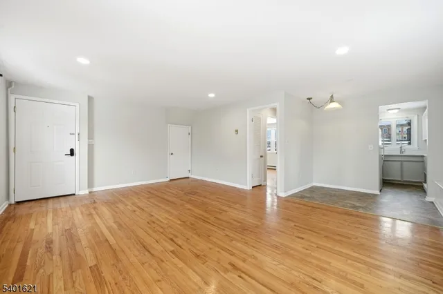 a view of empty room with wooden floor and kitchen
