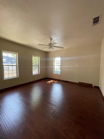 an empty room with wooden floor and windows with curtains