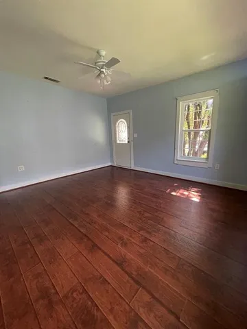 an empty room with wooden floor chandelier fan and windows