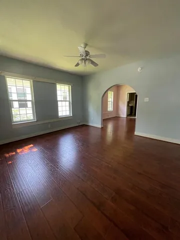 an empty room with wooden floor chandelier fan and windows