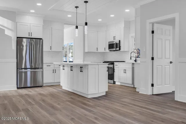 a kitchen with stainless steel appliances granite countertop a refrigerator a sink a stove and white cabinets with wooden floor