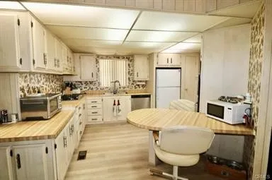a large kitchen with kitchen island a stove a sink a refrigerator and white cabinets with wooden floor