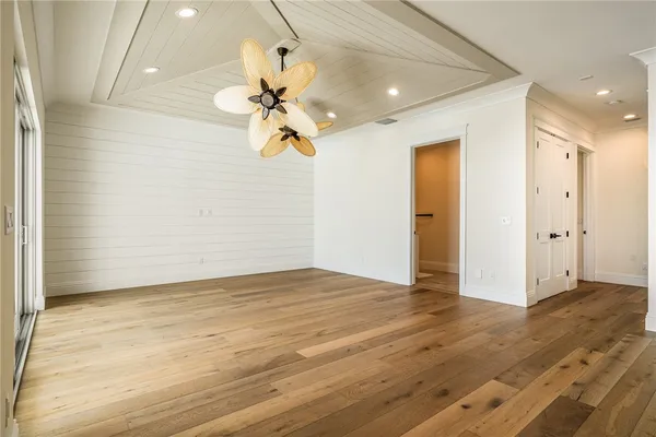 a view of an empty room with chandelier fan and wooden floor