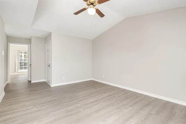 an empty room with wooden floor ceiling fan and windows