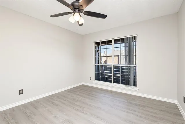 an empty room with wooden floor fan and windows