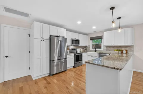 a kitchen with granite countertop a refrigerator a sink dishwasher a stove and white cabinets with wooden floor